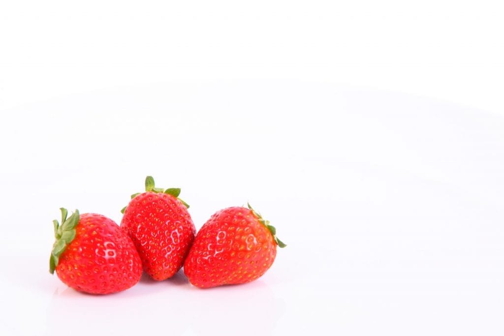 Three strawberries bright red on a white table shot in macro