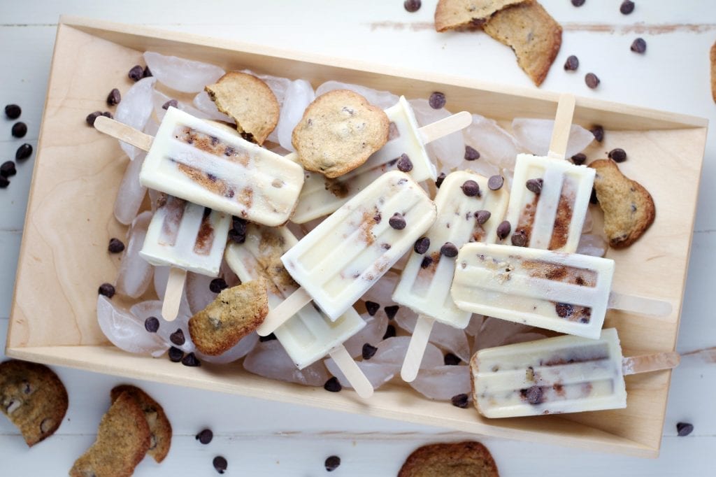 Oreo infused Popsicles with cookies and chocolate chips spread around them the Popsicles are on ice cubes in a wooden box