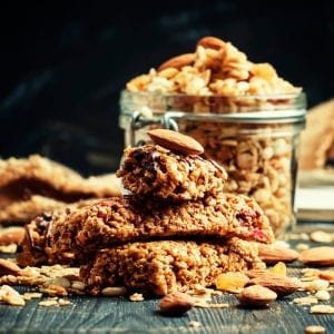 Cannabis infused cereal bars on a wooden table with a glass dish in the background that has more cereal bars in it