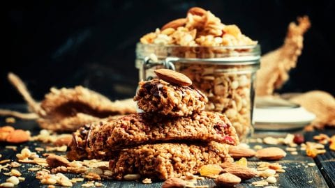 Cannabis infused cereal bars on a wooden table with a glass dish in the background that has more cereal bars in it