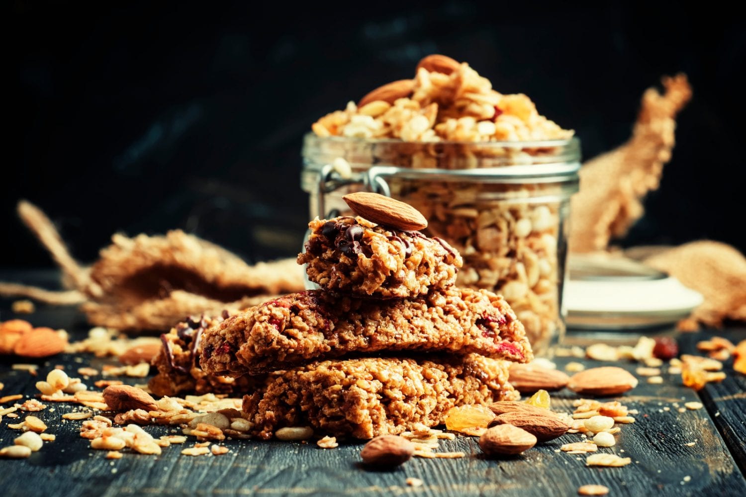 Cannabis infused cereal bars on a wooden table with a glass dish in the background that has more cereal bars in it