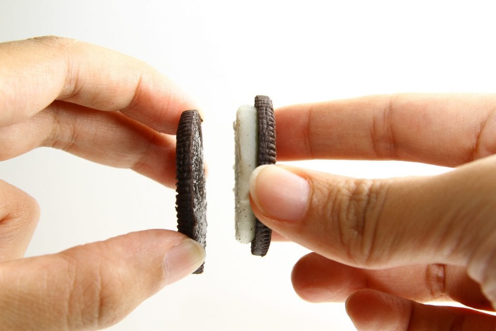 A persons hands pulling an oreo in half separating the two sides of the cookie. a weed chocolate covered oreo recipe. 