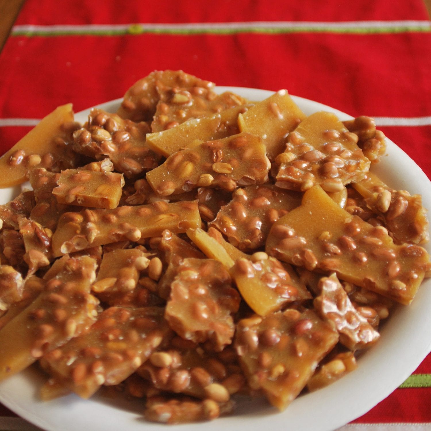 cannabis infused peanut brittle on a white plate which is all on a red tablecloth