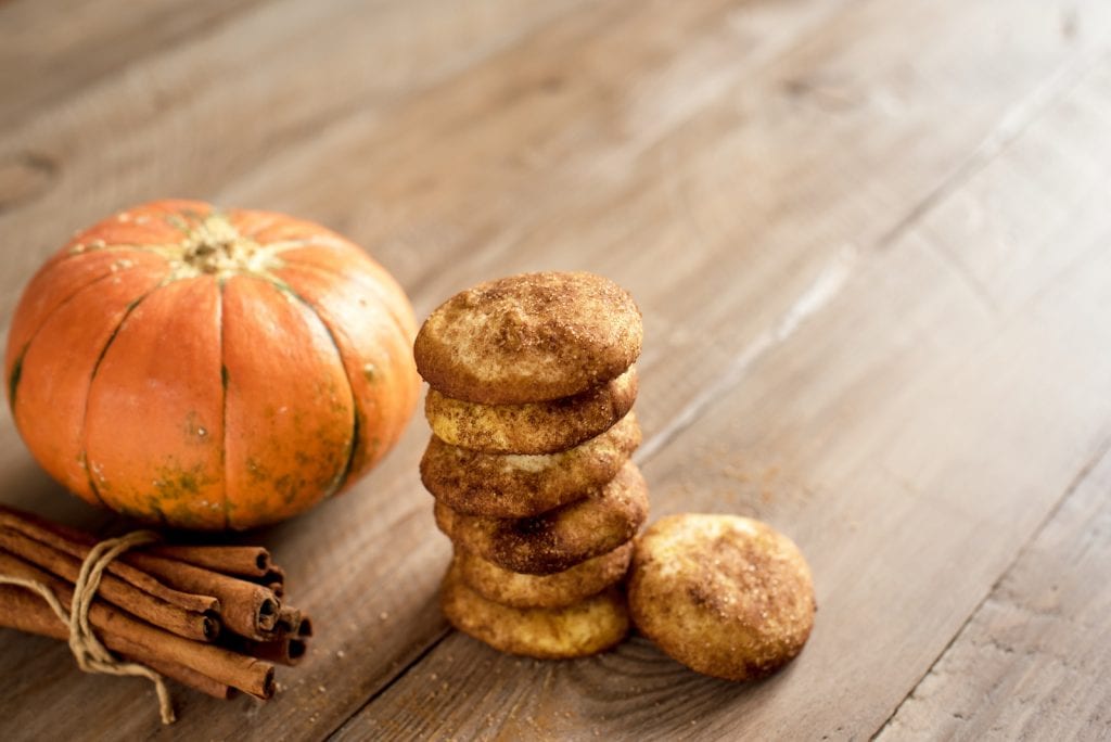 A stack of cannabis infused snickerdoodle cookies on a wooden surface with a pumpkin and cinnamon sticks in the background