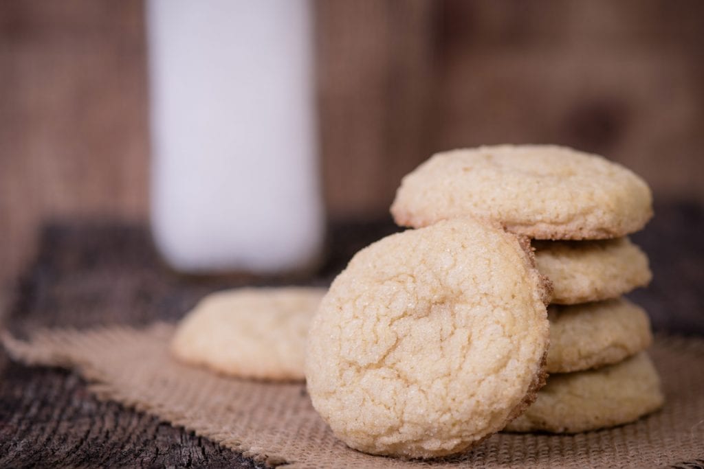 a stack of weed sugar cookies on a rustic wooden surface with more sugar cookies around the stack