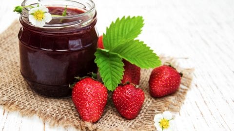 weed strawberry jam in a glass jar with strawberries beside the jar.