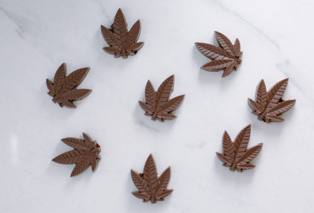 cannabis leaf shaped chocolates on a white marble counter.