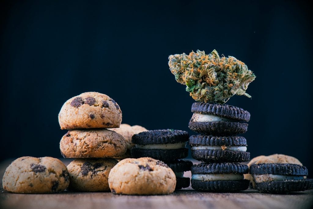 Cannabis nug on top of infused oreo cookies and chocolate cookies on a wooden table. 