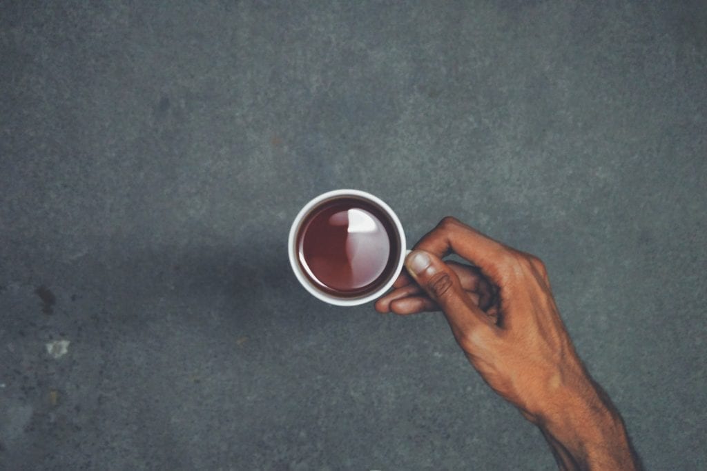 Mans hand holding a mug with weed tea in it over a black surface. 