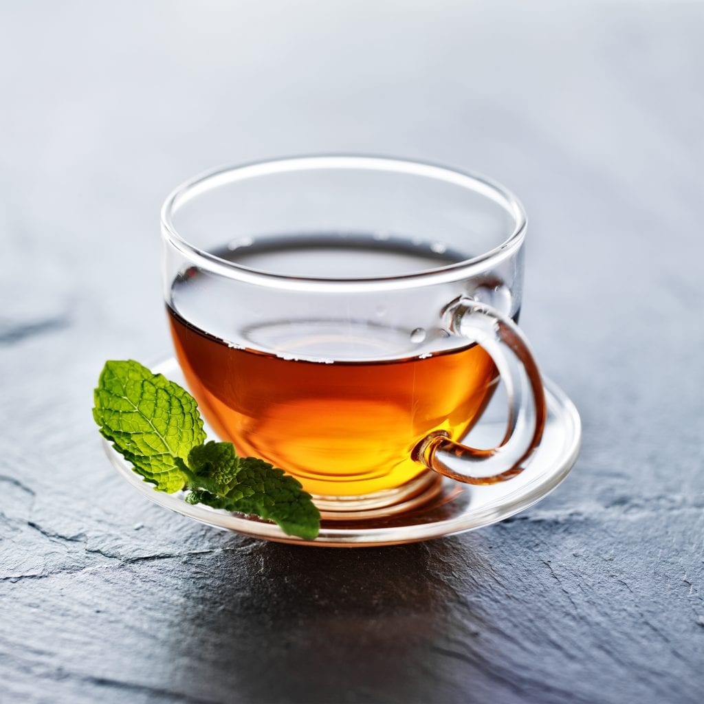 glass of hot tea with mint garnish on a white plate used for at home remedies