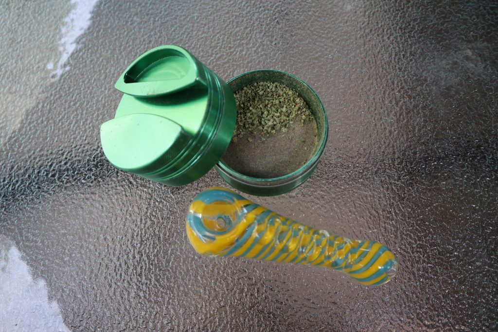 A green grinder and glass weed pipe on a glass table. 