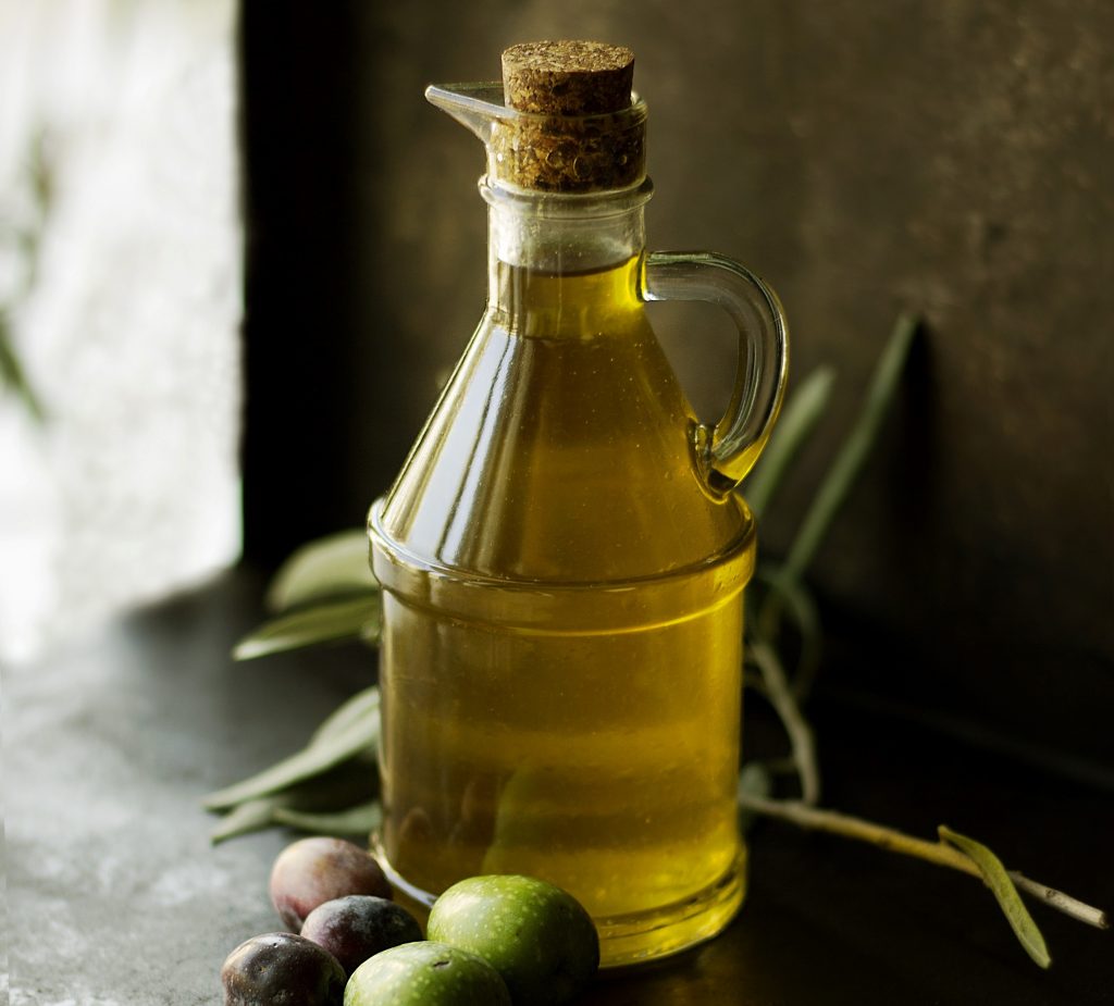 CBD-infused cooking oil in an airtight glass jar. Fruits sit in front of the jar with grass behind it.