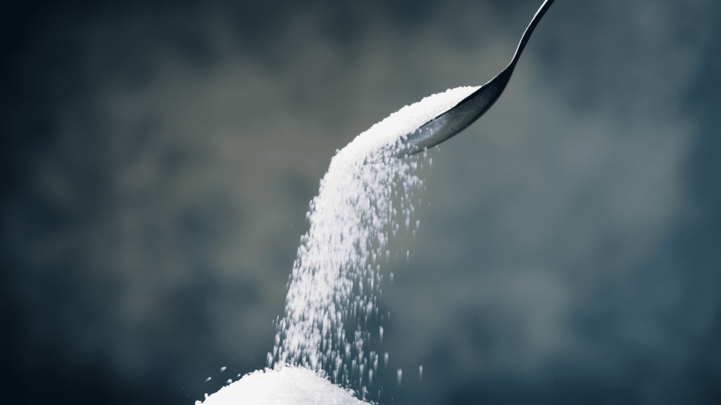 CBD-infused sugar falling off of a metal spoon. The small grains of white sugar make a pile.