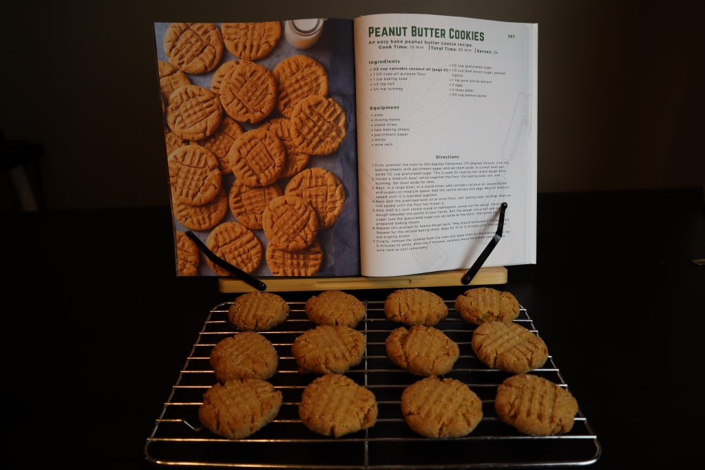 weed peanut butter cookies on a wire rack in front of a cannabis cookbook on a black table.