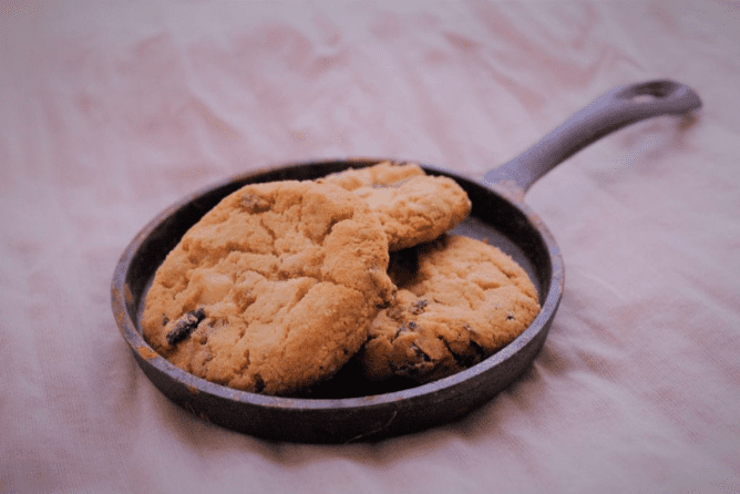 Small cast iron pan with 3 cannabis cookies artistically place on top of each other with purple background 